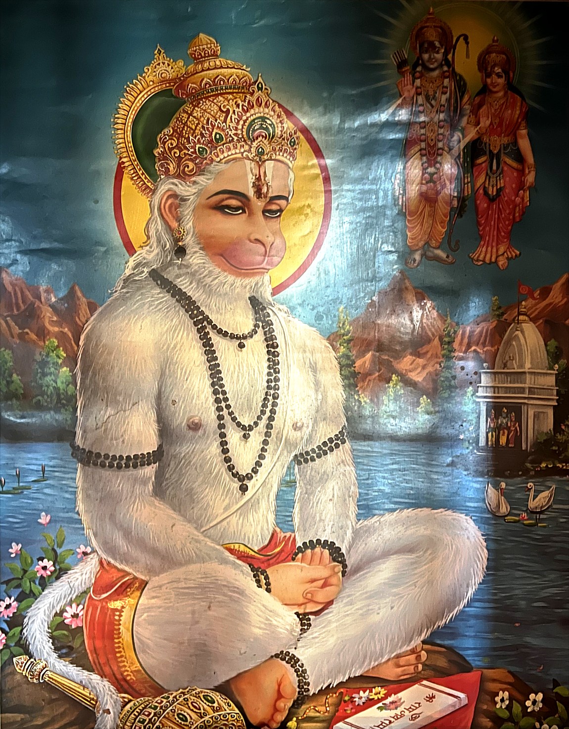 Hanuman seated in meditation by the water, wearing a rudraksha mala, with Rama and Sita appearing above